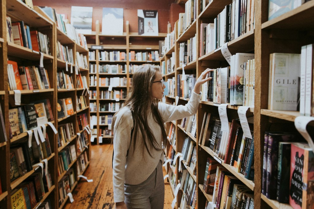 A woman looks through books on a bookshelf in a book shop.