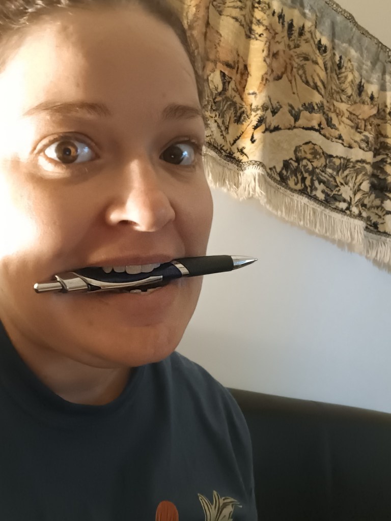jess smiling at the camera with a pen in her mouth